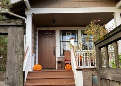 A cozy front porch adorned with two pumpkins, leading up to a wooden front door with stairs and a surrounding wooden fence.