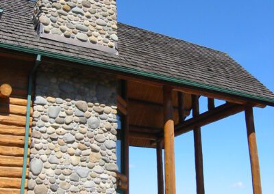 Log cabin with a stone chimney under a clear blue sky.