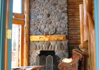 Rustic cabin interior with a stone fireplace and a wooden bench.