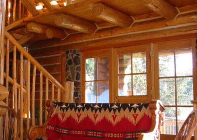 Warm sunlight streams into a cozy log cabin living room with rustic wooden furniture and a patterned sofa.