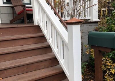 Wooden stairs with white railings leading to a house entrance with a green mailbox on the side and scattered leaves.