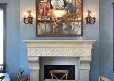 Elegant dining area with a marble fireplace, antique-style chairs, a crystal chandelier, and a framed artwork above the mantel.