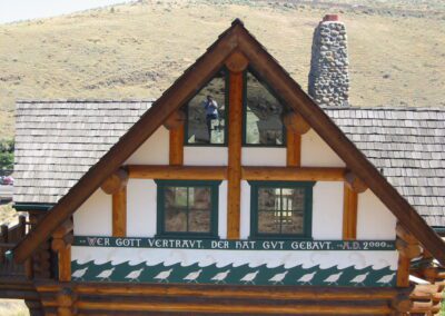 A log cabin with a distinctive triangular facade, wooden shingles, and a german inscription that translates to "who trusts in god has built well. a.d. 2000.