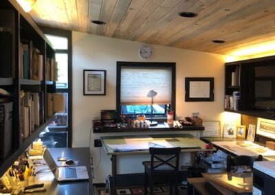Cozy home office with wooden ceiling, bookshelves, and a desk with a lamp.
