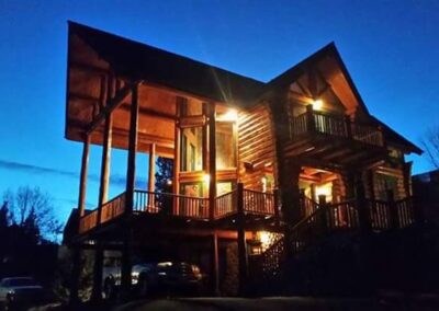 A log cabin illuminated by exterior lights against a twilight sky.