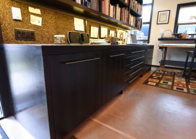 A modern home office with a dark wooden desk, bookshelves, and a patterned area rug.