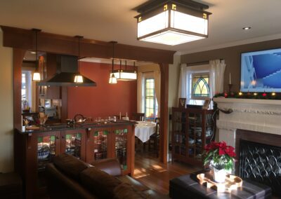 A cozy living room with craftsman-style interiors, featuring a fireplace, hanging light fixtures, and a view into the dining area.