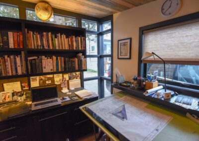 A home office with a laptop, bookshelves, drafting table, and various office supplies.
