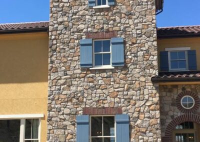 Three-story house with stone facade and blue window shutters under a clear sky.