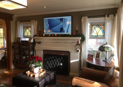 A cozy living room decorated for the holidays with a fireplace, a mounted television, and classic windows.