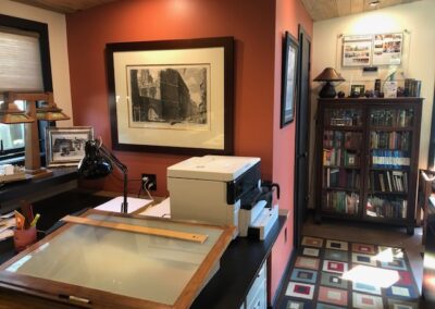 A home office with a large desk, bookshelf, and framed artwork on the walls.