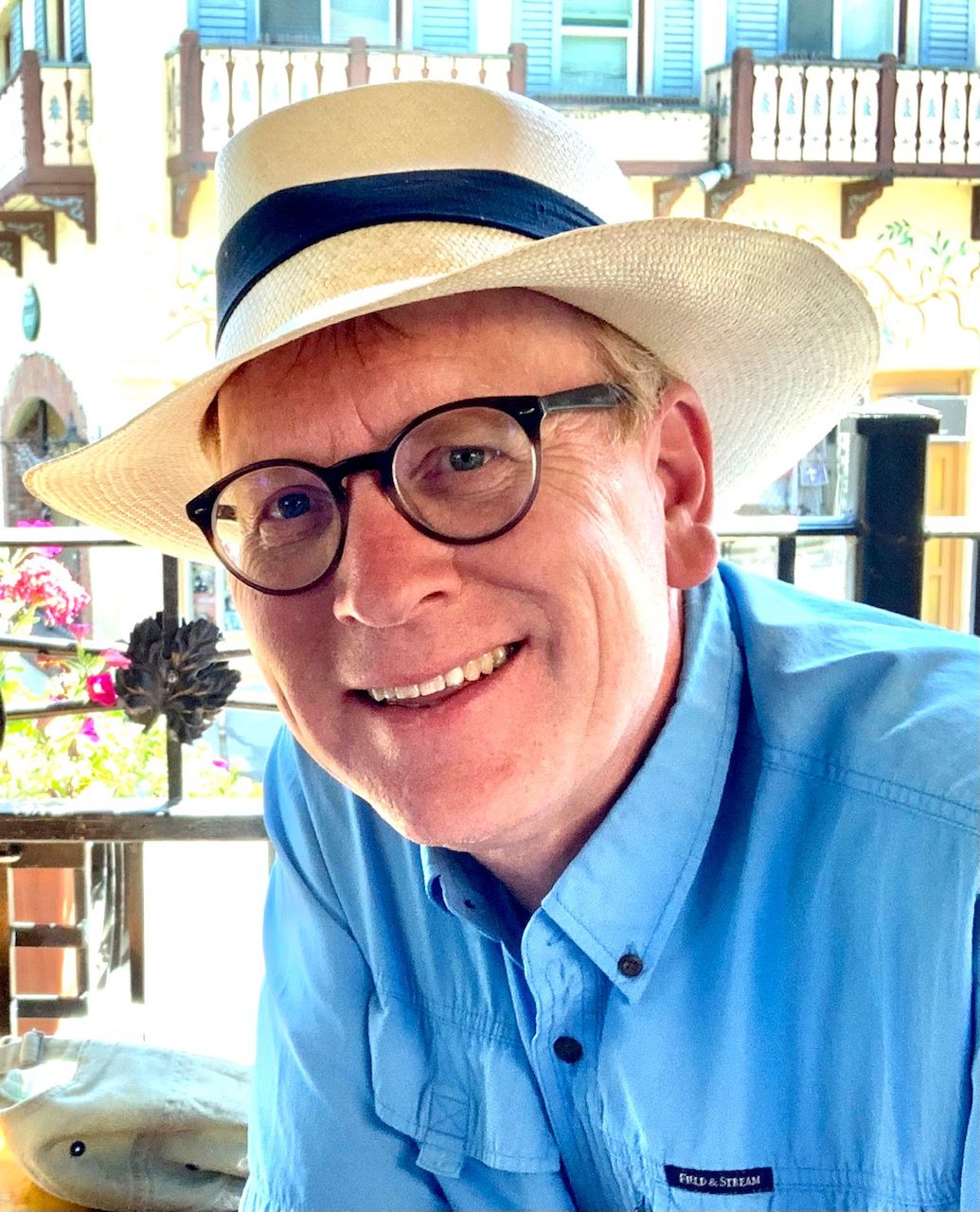 Man wearing glasses and a straw hat smiling at the camera.