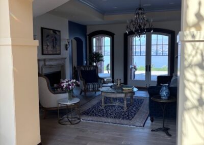 A well-lit living room with armchairs, a sofa, a coffee table, and a chandelier, featuring large French doors opening to a view outside.