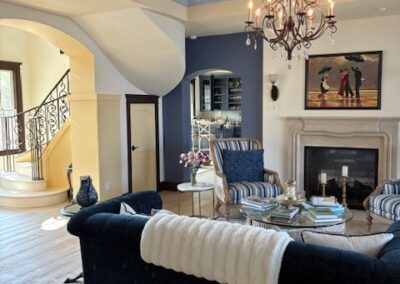 Elegant living room with a black sofa, striped chairs, fireplace, chandelier, spiral staircase, and wall art in a spacious, well-lit space with light wood floors and blue accent walls.